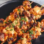 Bang Bang Chicken Skewers grilled and served on a black plate with garnish