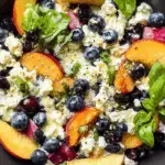 Blueberry Peach Feta Salad in a black bowl with fresh basil