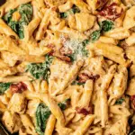Bowl of creamy tuscan chicken pasta garnished with basil and parmesan on a wooden table