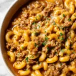 Delicious homemade hamburger helper served in a rustic bowl topped with melted cheese and garnished with parsley.